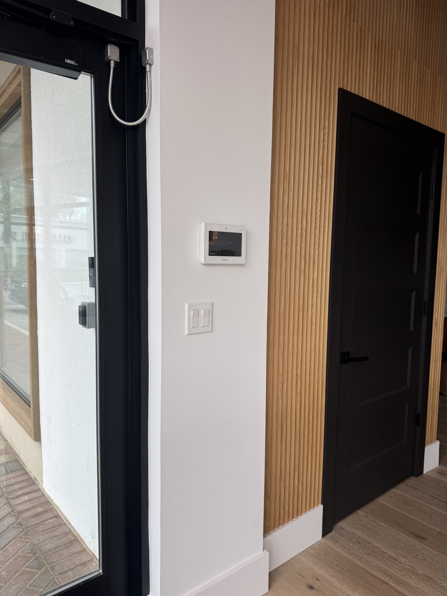 Alarm system keypad and light switch panel mounted near the interior entry door in East Hills, NY