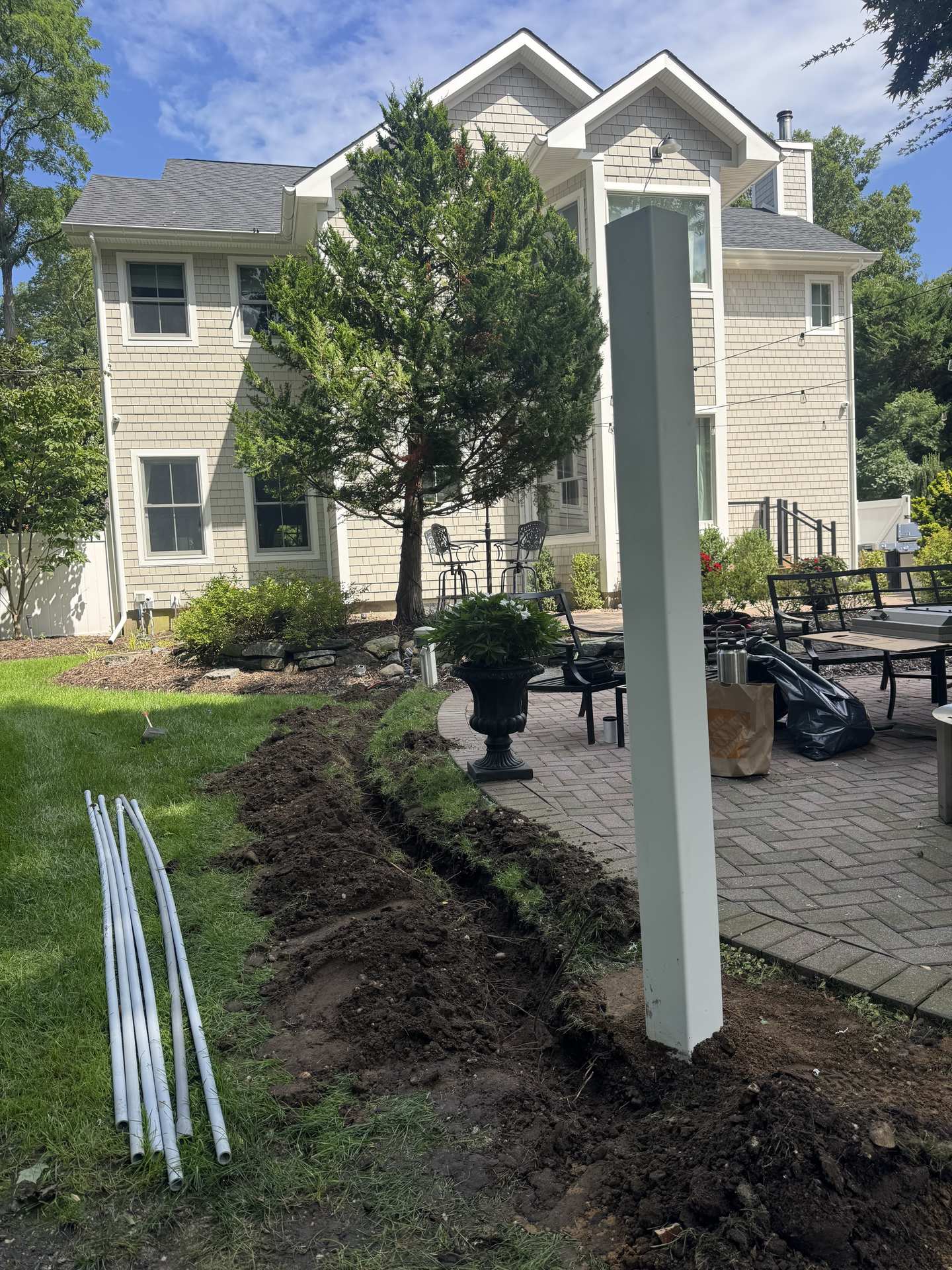 Trenching and white PVC conduit pipe laid across a Northport, NY lawn for an outdoor TV installation